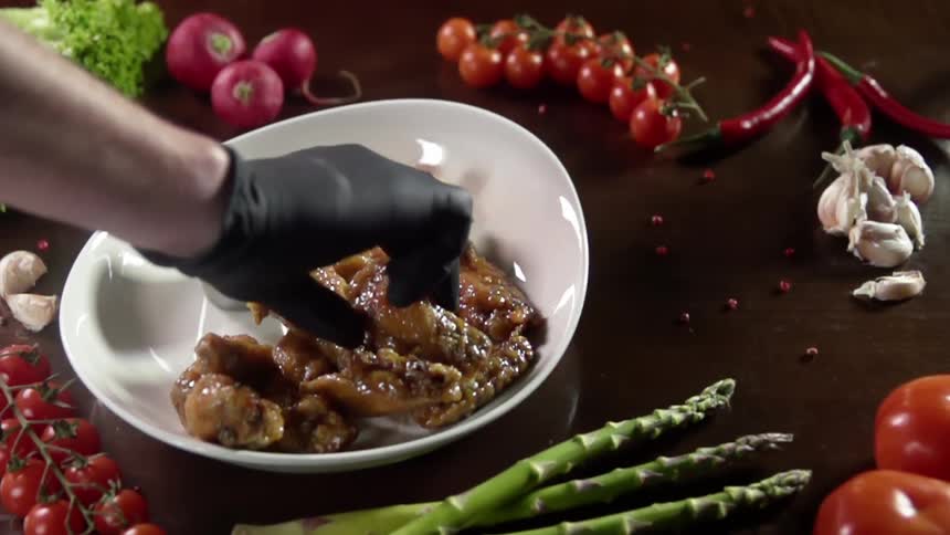 Chef wearing black latex gloves picks fried chicken from a white ceramic plate