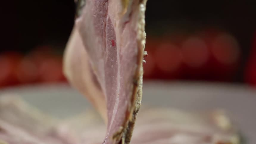 A single slice of ham is slowly lowered onto a plate with other pieces of ham on it