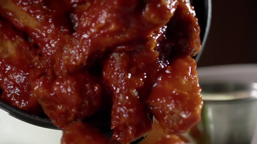 Chicken wings covered in sauce being pushed out of a pan with a mixing spoon