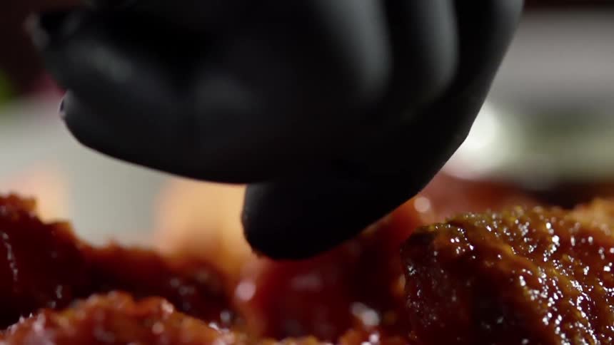 A person wearing a black glove lifts a piece of food out of a bowl