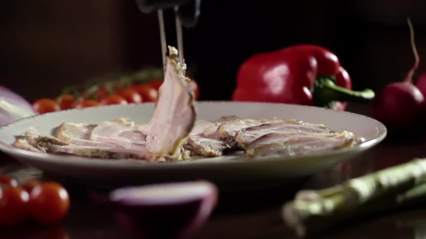 Tongs place sliced meat on to a plate surrounded by fresh red peppers