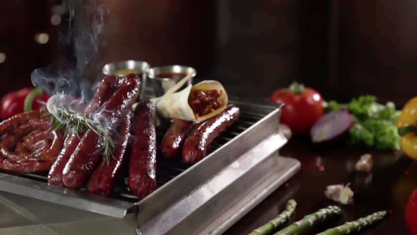 A smoking vegetable falls onto a pile of sausages on a grill