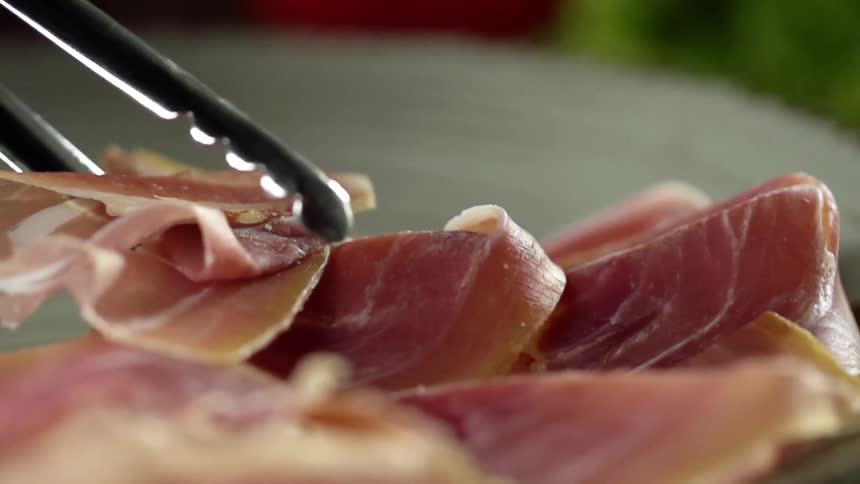 Narrow tongs place sliced ham onto white plate