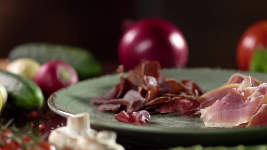 Bacon pieces dropping next to ham slices in slow motion on a plate