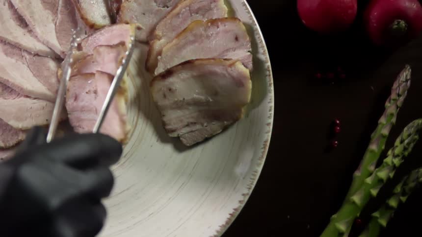 Chef wearing black latex gloves places sliced of pork belly over a ceramic white plate