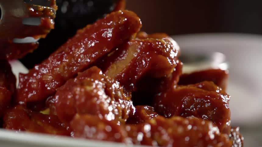 Several pieces of cooked meat covered in a reddish brown sauce are poured onto a plate