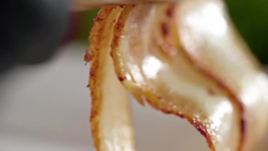 Cooked bacon strips served in a white plate using tongs