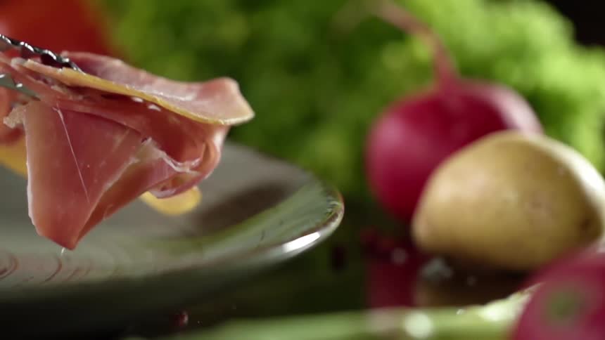 Slices of prosciutto placed in a ceramic dish near vegetables