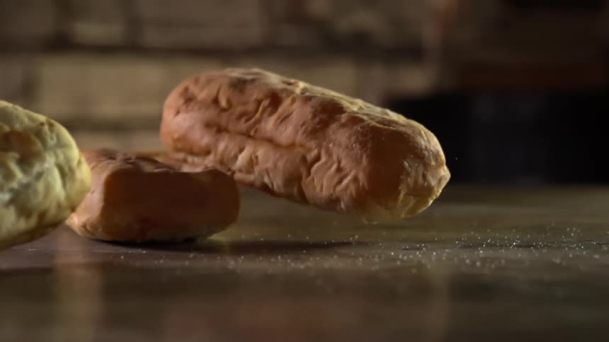 Three baked rolls are dropped onto a flat counter top where they bounce and then come to a rest