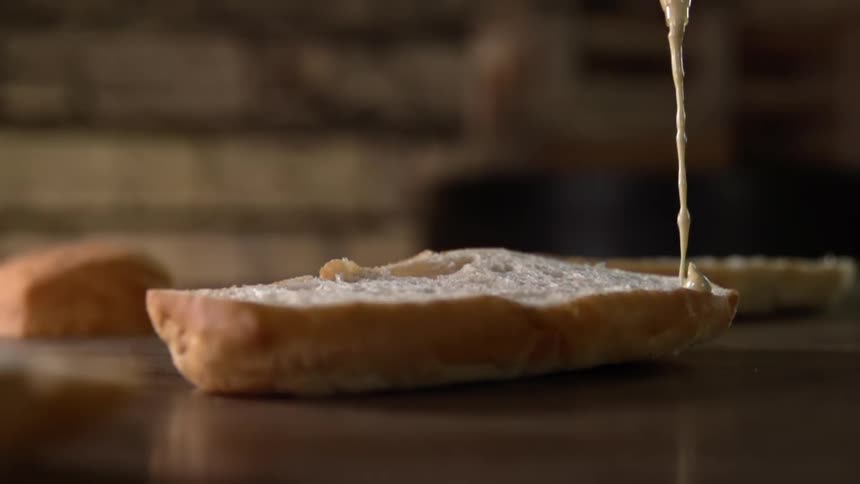Mayonnaise squirts over sliced bread in a counter top