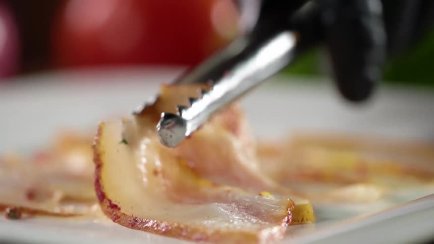 A person drops a slice of meat on a plate with metal tongs