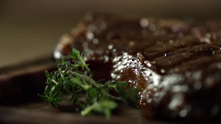 A small piece of parsley is dropped next to a perfectly grilled piece of steak on a plate