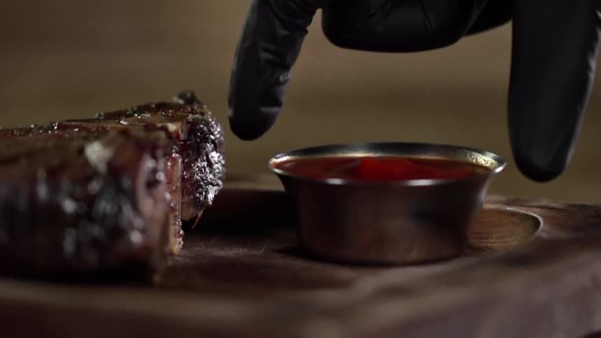 A person sets sauce on a wooden platter next to meat