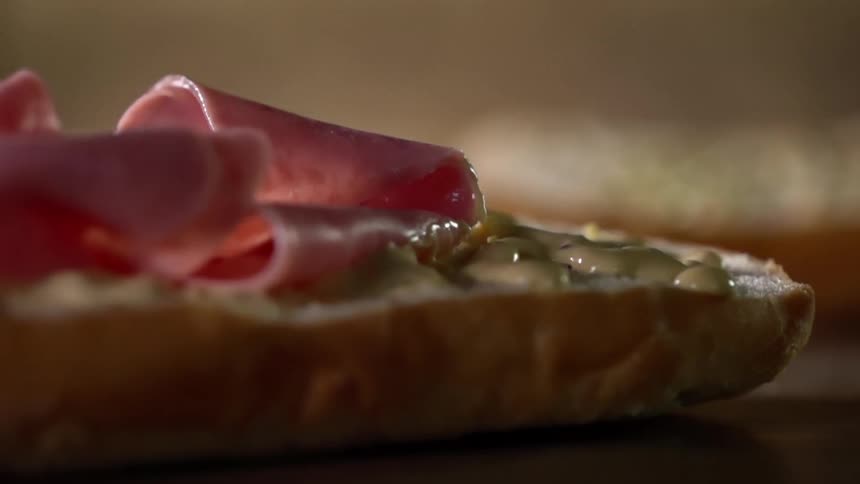 Ham falling on to a bun with mustard on it