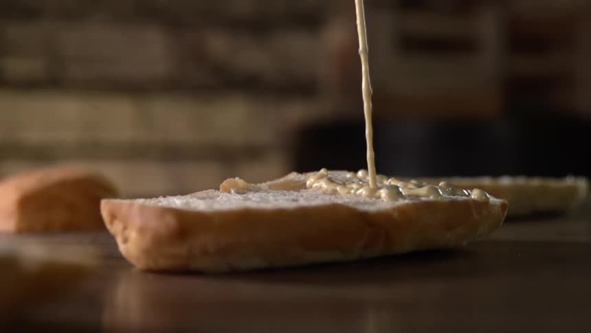 Mustard is being sprayed on he bread