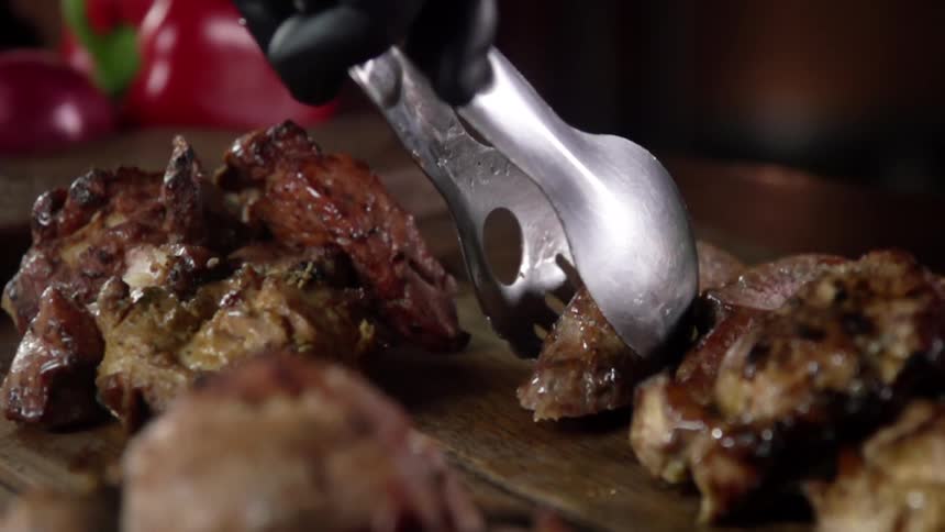 Grilled pieces of meat placed over a wooden board with pliers