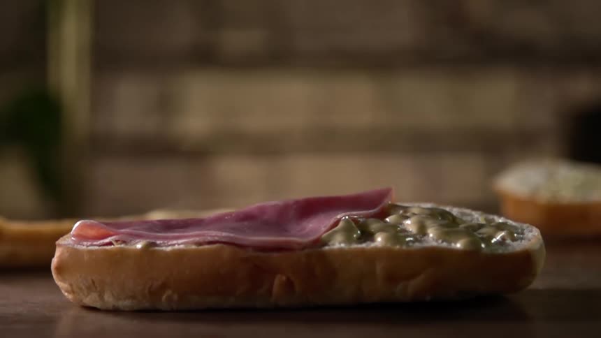 A piece of ham falls on bread with a spread on it