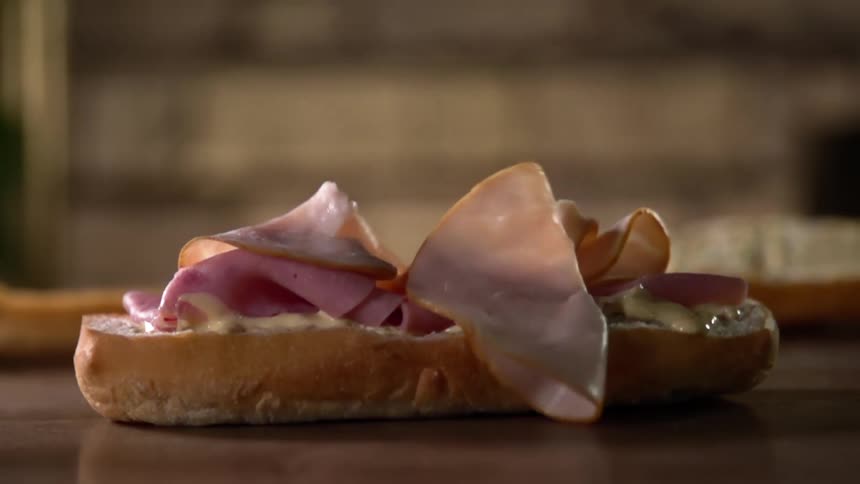 Sliced meat drops onto a piece of bread on a table