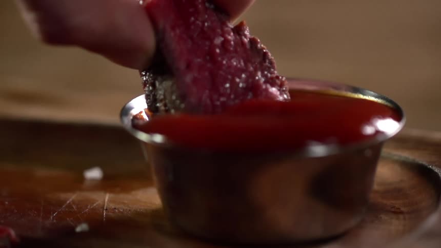 A hand dips a slice of steak into ketchup