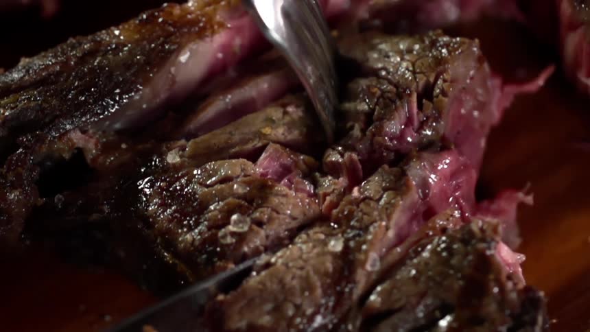 A white person cuts a piece of under cooked steak with a knife and fork