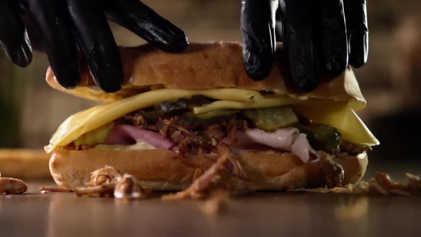 Gloved hands lower a slice of bread on to the top of a sandwich