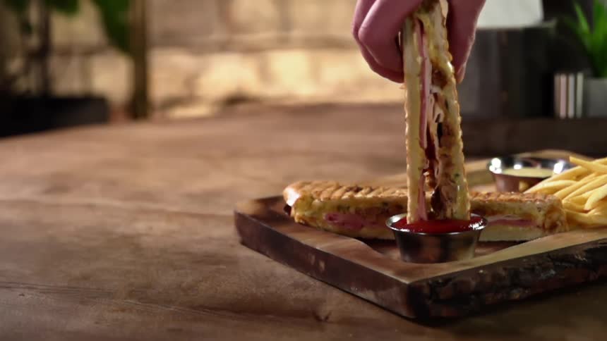 Half of a panini sandwich is dipped into a ramekin of ketchup