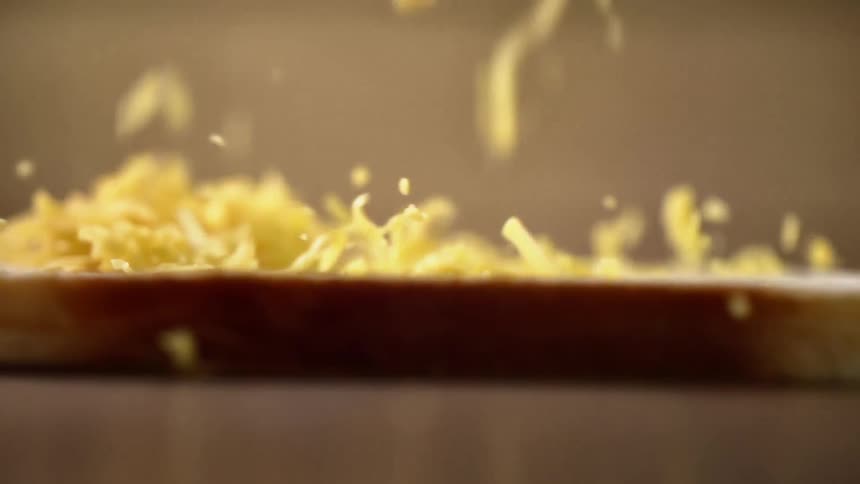 Grated yellow cheese falling on a slice of bread