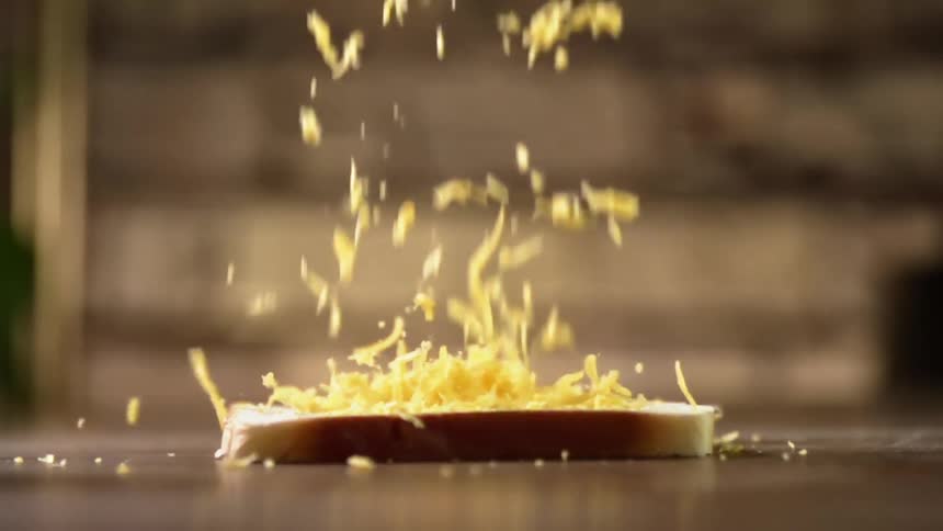 Yellow shredded cheese pours over a slice of bread