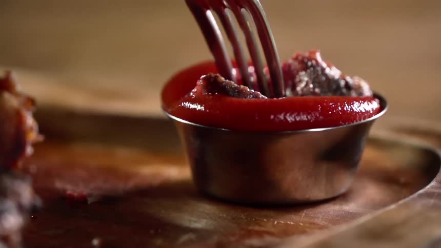 A fork dips a piece of steak in sauce