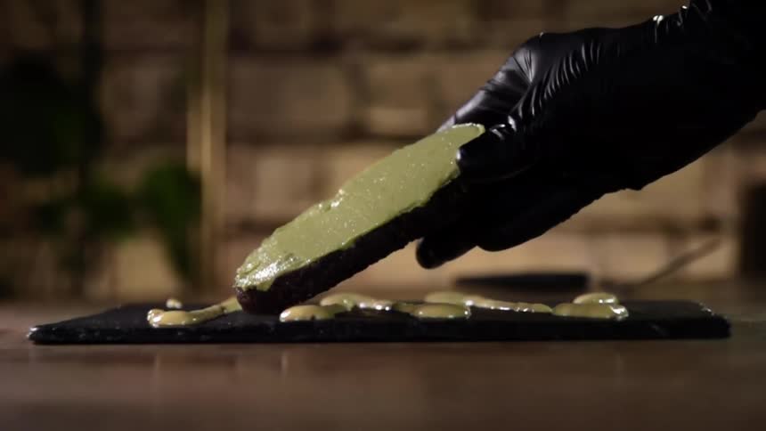 Chef wearing black latex gloves places a slice of bread covered in cream over a plate
