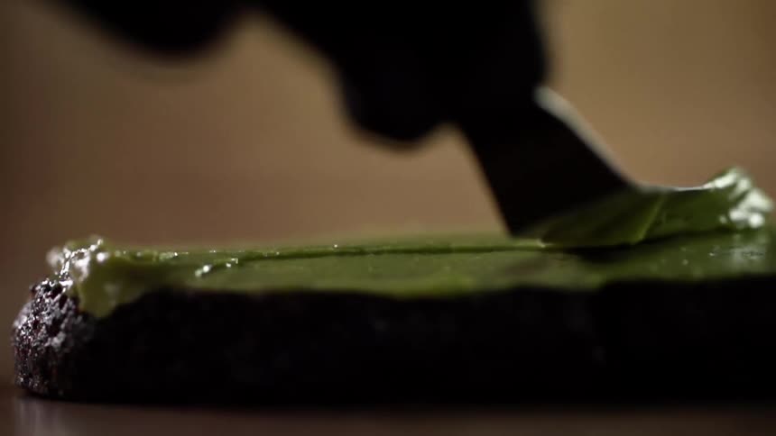 Chef wearing black latex gloves spreads green paste over a plate with a spatula