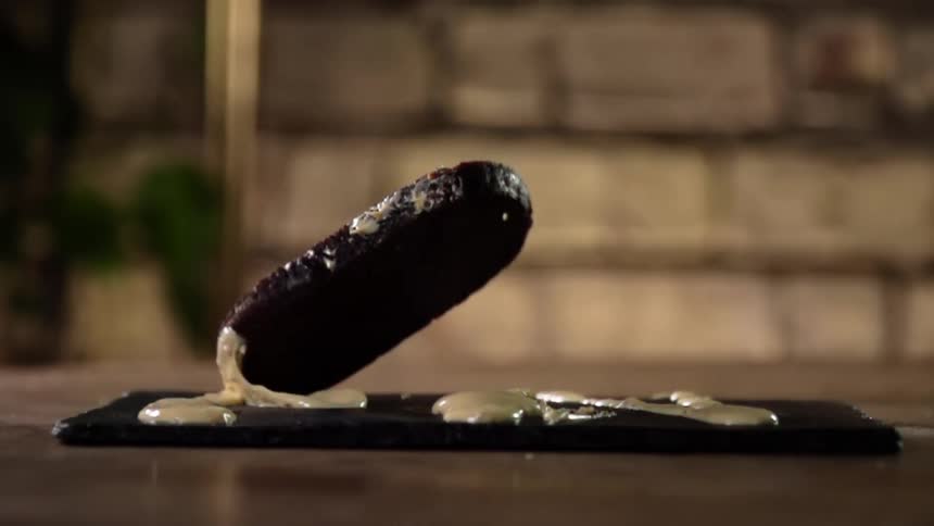 A piece of dark bread drops on a platter covered in sauce