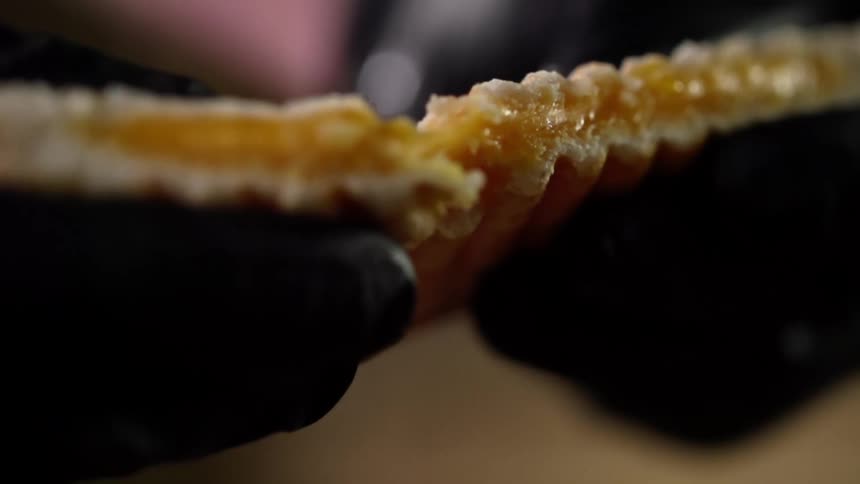 Person in black gloves tears filled pastry in half