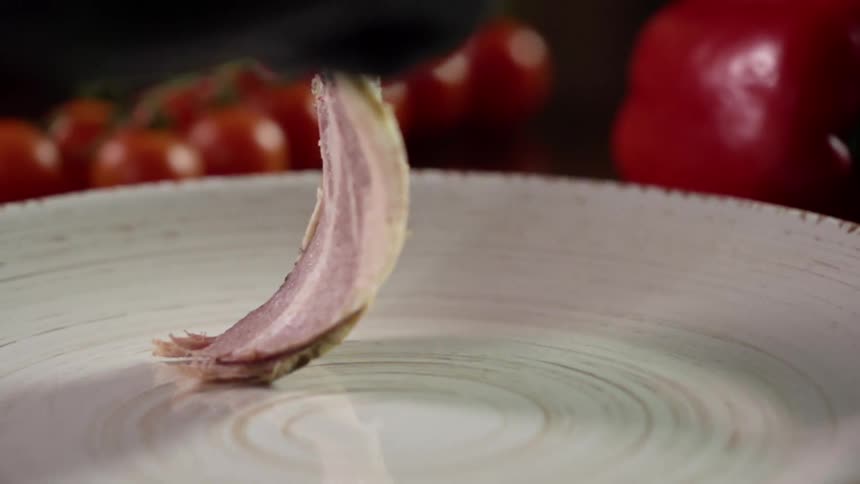 A hand in a black glove sets slices of meat on a plate