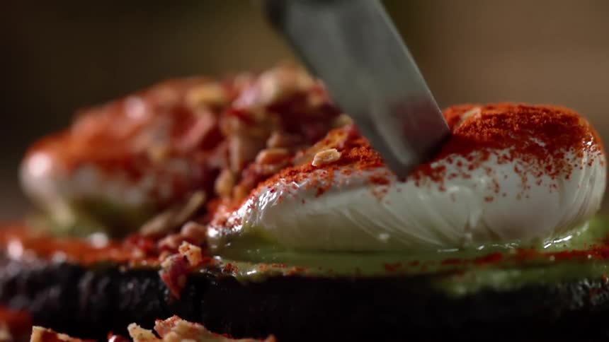 Poached eggs covered in red paprika being sliced with a sharp kitchen knife