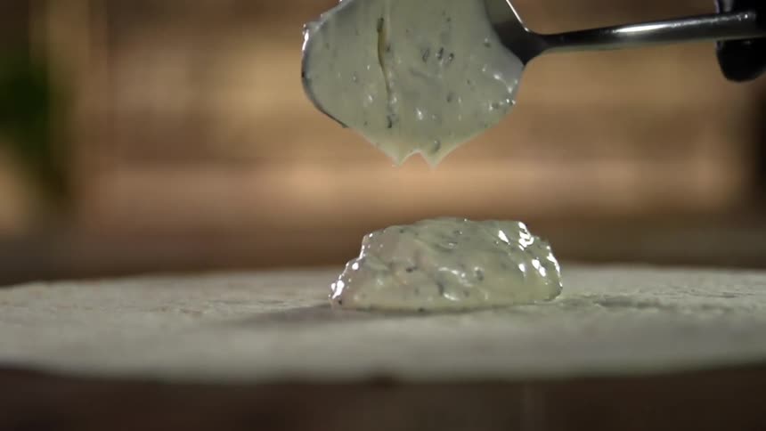 A person drops a spoonful of light green sauce onto a tortilla