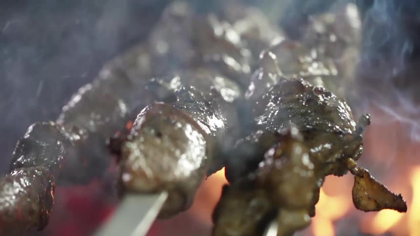 Meat is cooked on skewers over a smoky grill