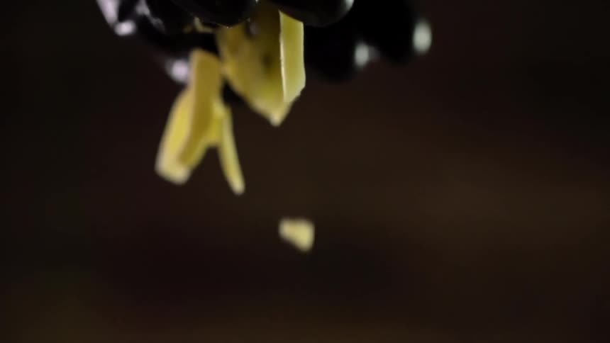 A person wearing a black glove sprinkles shredded cheese