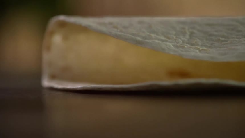 A flour tortilla folds in half as its dropped onto a counter