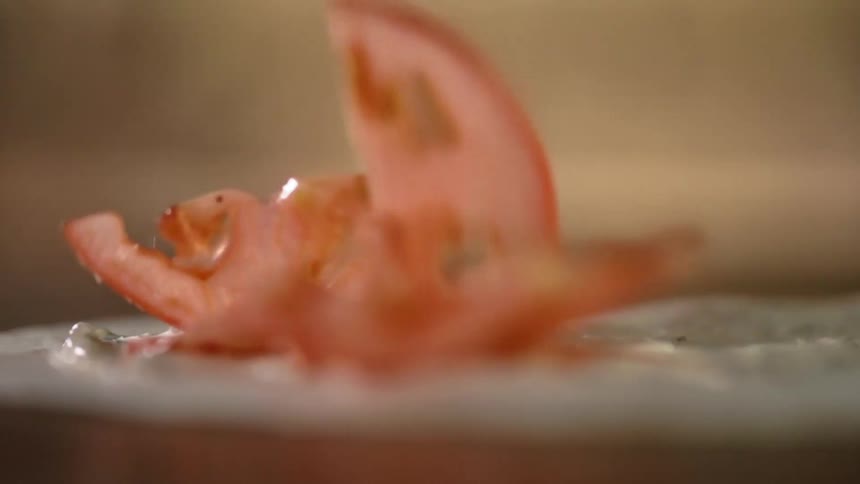 Close up of tomato slices falling on wrap with sauce