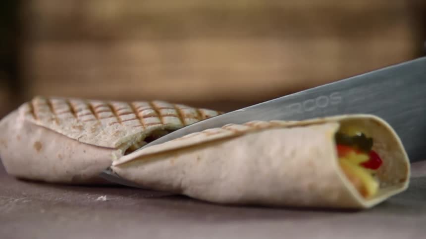 Sharp knife cutting grilled burrito in half in slow motion