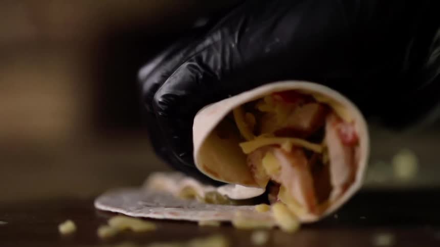 A gloved hand turns a wrap filled with meat and corn chips