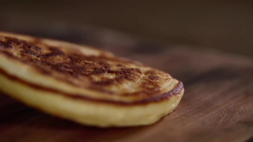 Golden brown flour pancake being placed over a wooden board