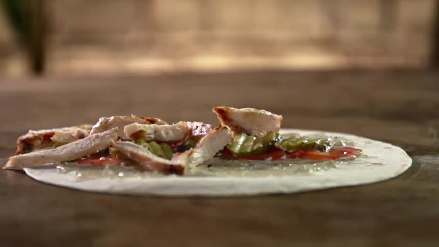 Strips of cooked chicken are dropped onto a white tortilla with sauce and toppings
