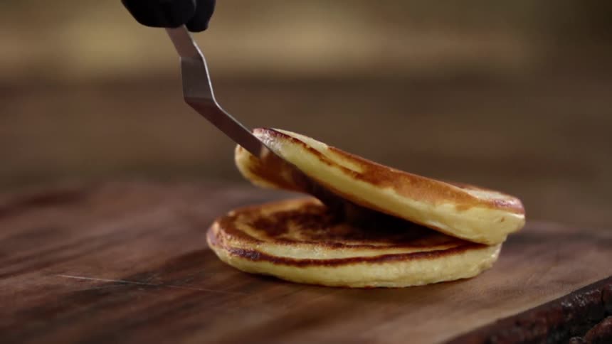 A hand in a black glove sets a pancake down on top of another pancake