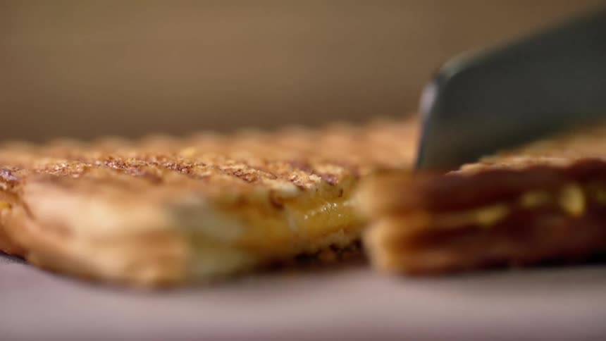 Close up of a hand wearing a black glove cutting a toasted sandwich with a bread knife