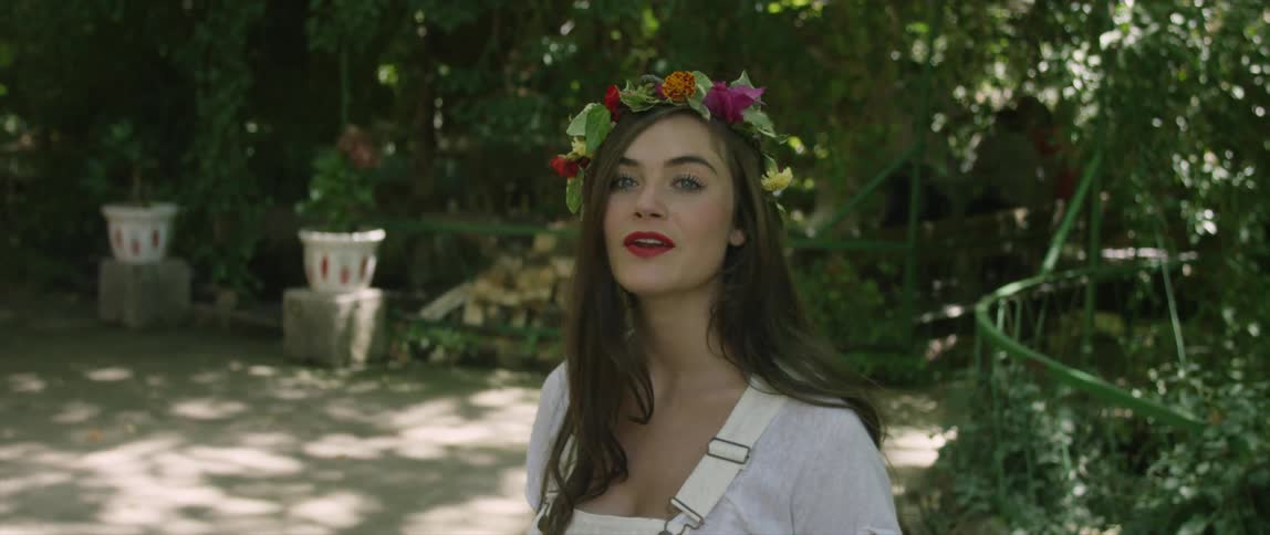 A smiling woman wearing a crown of flowers in her hair speaks to someone