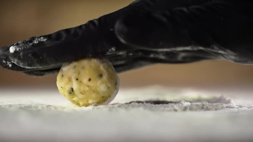 Chef wearing black latex gloves rolls a ball of food over flour in a table