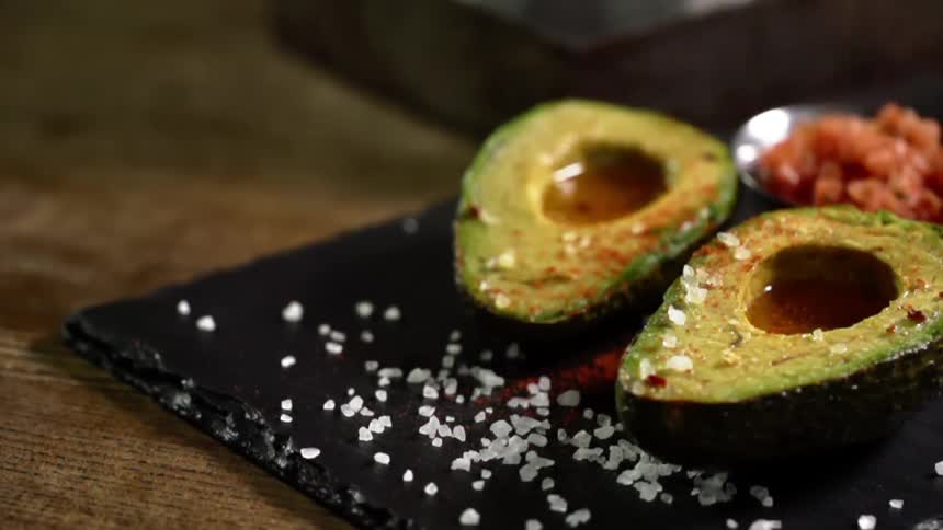 Seasoning is sprinkled onto a cut avocado