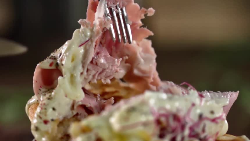 A fork pulls up slices of ham after a breakfast sandwich is cut through